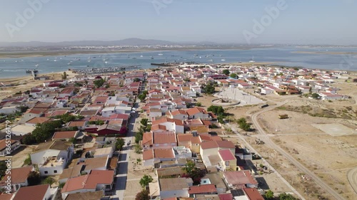 Simple brown orange roof homes with anchored boats in channel, establishing aerial of Culatra Island Olhao Portugal
