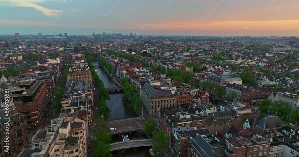 Aerial view of the European tourist city of Amsterdam. A drone flies over the city center at sunset. Establishing shot of the main and famous city in the Netherlands. Narrow canals divide the city Aerial view of the European tourist city of Amsterdam. A drone flies over the city center at sunset. Establishing shot of the main and famous city in the Netherlands. Narrow canals divide the city