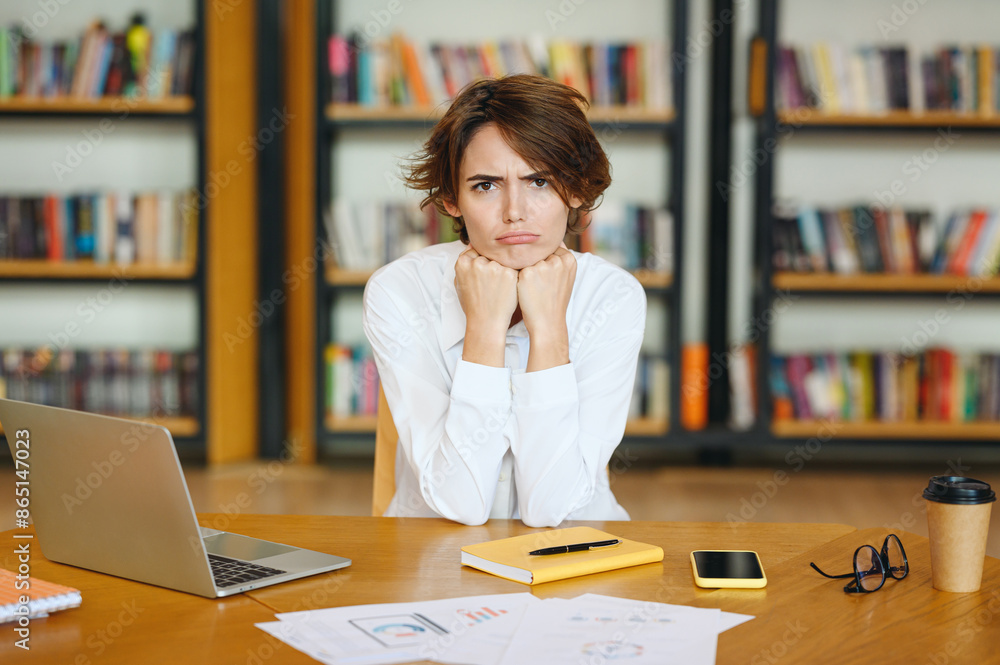 Young sad mad upset upset dissatisfied displeased employee business woman wear white shirt casual clothes prop up chin look camera sit work at office desk with pc laptop. Achievement career concept. Young sad mad upset upset dissatisfied displeased employee business woman wear white shirt casual clothes prop up chin look camera sit work at office desk with pc laptop. Achievement career concept.