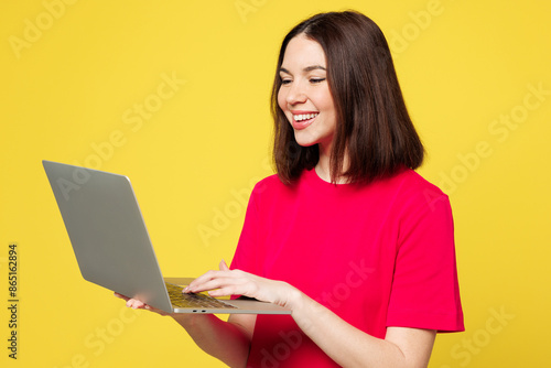 Side view young smart IT woman she wear pink t-shirt casual clothes hold use work on laptop pc computer chatting online isolated on plain yellow orange background studio portrait. Lifestyle concept.