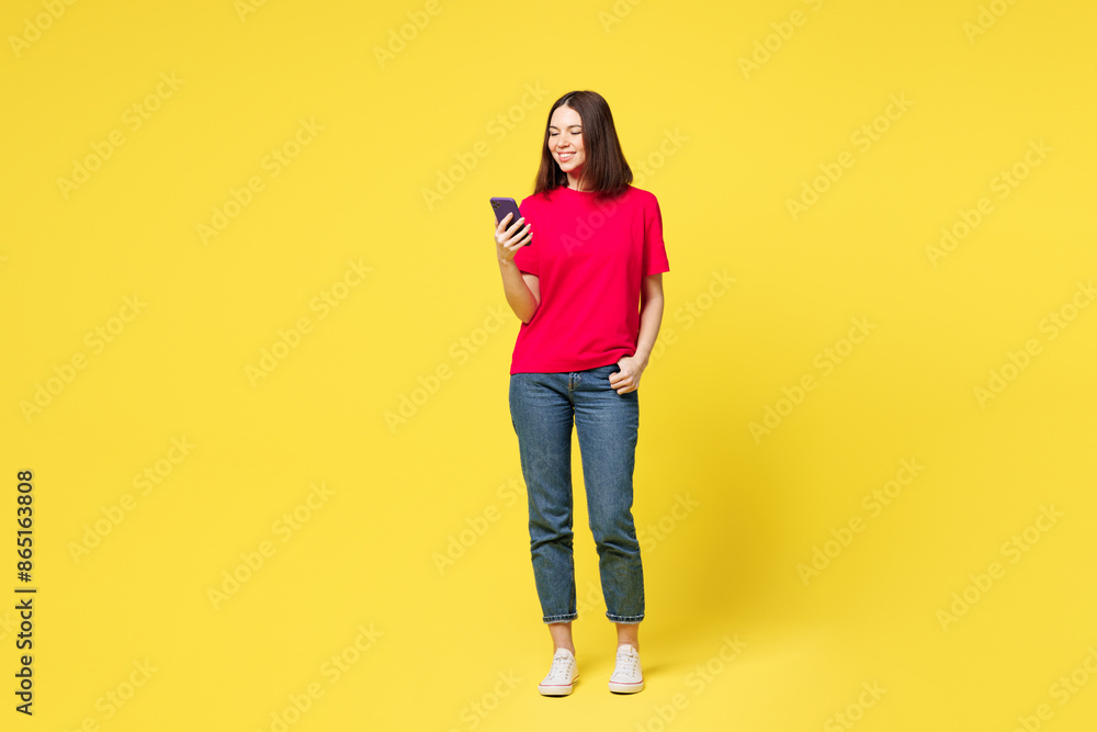 Full body young student fun woman she wear pink t-shirt casual clothes hold in hand use mobile cell phone chatting online isolated on plain yellow orange background studio portrait. Lifestyle concept. Full body young student fun woman she wear pink t-shirt casual clothes hold in hand use mobile cell phone chatting online isolated on plain yellow orange background studio portrait. Lifestyle concept.