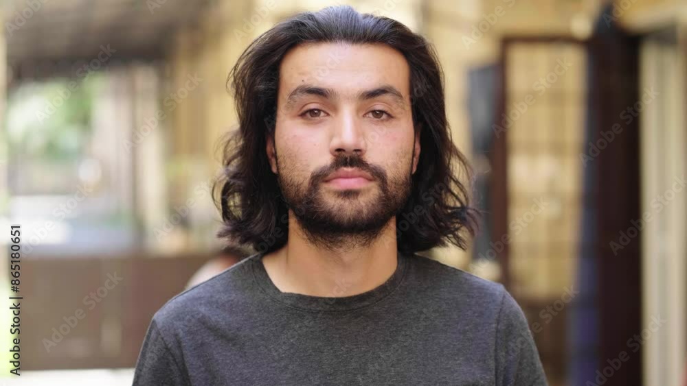 A young man in his 30s with long black hair and an unkempt beard looks seriously at the camera, reflecting deep thought and intensity in his expression. A young man in his 30s with long black hair and an unkempt beard looks seriously at the camera, reflecting deep thought and intensity in his expression.