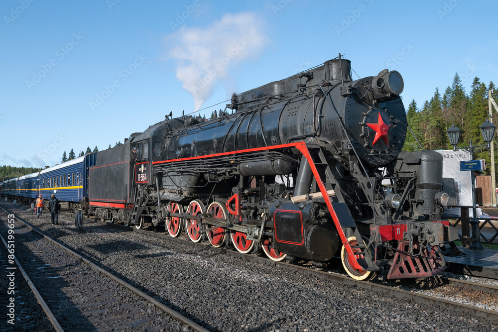 The old steam locomotive L-5164 with the retro train on the Ruskeala Mountain Park station on a sunny October day. Karelia The old steam locomotive L-5164 with the retro train on the Ruskeala Mountain Park station on a sunny October day. Karelia
