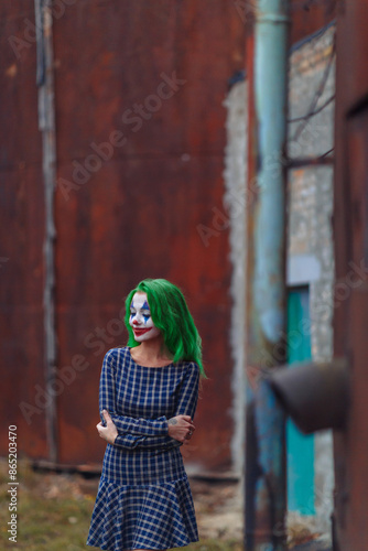 Portrait of a greenhaired girl in chekered dress with joker makeup on a rusty metal wall background.