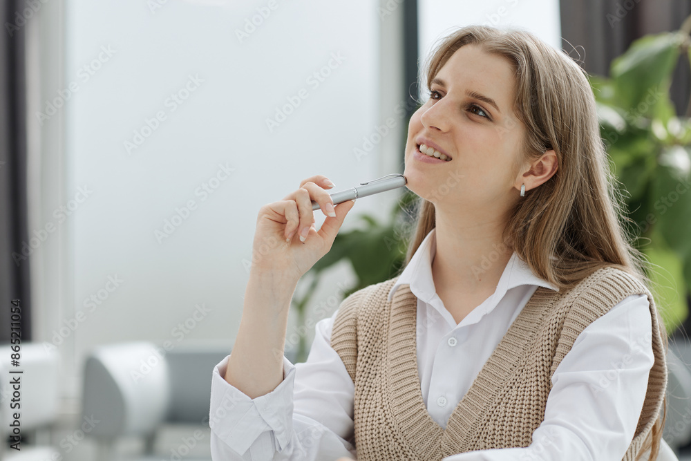 A beautiful young girl in the office works with documents, holds a pen in her hand and looks at the camera.