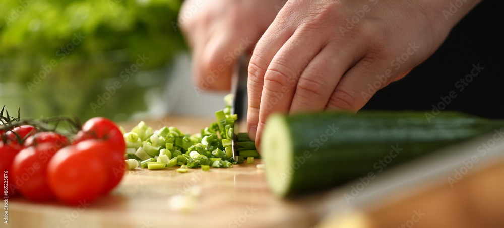 Cook holds knife in hand and cuts on cutting board green onions for salad or fresh vegetable soup with vitamins. Raw food and vegetarian recipe book in modern society popular concept. Cook holds knife in hand and cuts on cutting board green onions for salad or fresh vegetable soup with vitamins. Raw food and vegetarian recipe book in modern society popular concept.