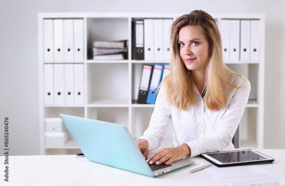 Beautiful businesswoman portrait in office sitting at table smiling and looking at camera teacher expresses success checking control papers Beautiful businesswoman portrait in office sitting at table smiling and looking at camera teacher expresses success checking control papers