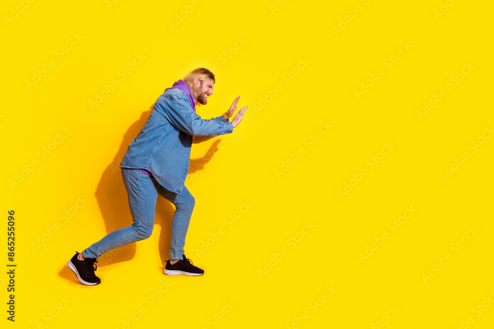 Full length profile portrait of nice young man push empty space wear denim jacket isolated on yellow color background Full length profile portrait of nice young man push empty space wear denim jacket isolated on yellow color background