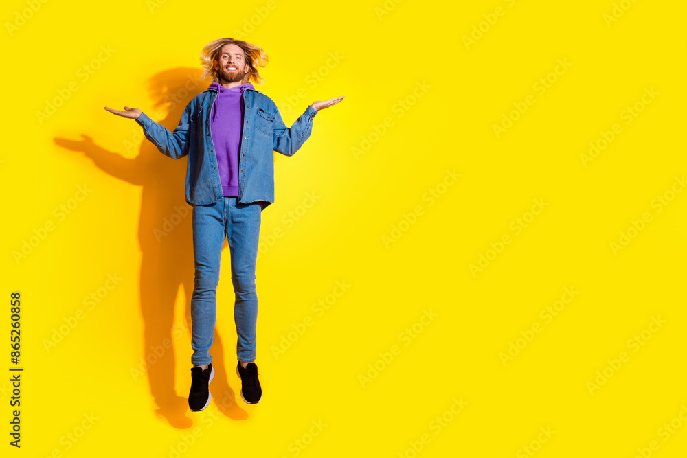 Full length portrait of nice young man jump hold empty space vs wear denim jacket isolated on yellow color background Full length portrait of nice young man jump hold empty space vs wear denim jacket isolated on yellow color background