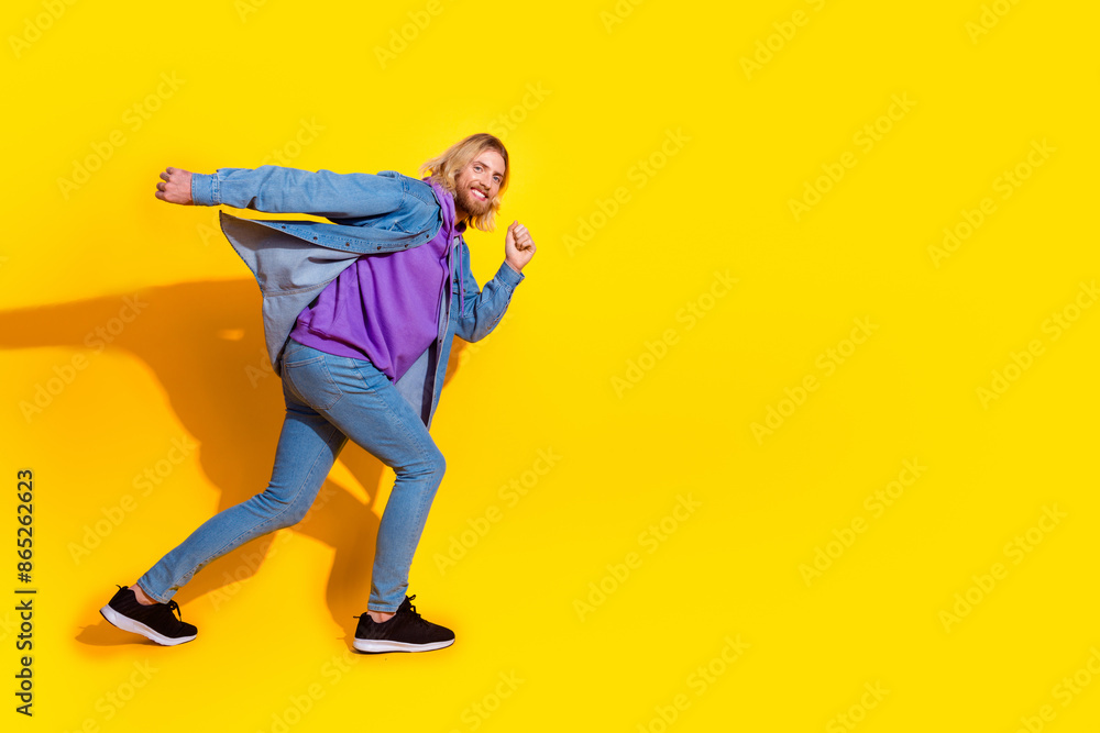 Full length profile portrait of nice young man run empty space wear denim jacket isolated on yellow color background Full length profile portrait of nice young man run empty space wear denim jacket isolated on yellow color background