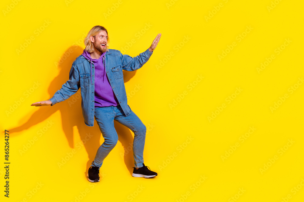 Full length portrait of nice young man dancing empty space wear denim jacket isolated on yellow color background Full length portrait of nice young man dancing empty space wear denim jacket isolated on yellow color background