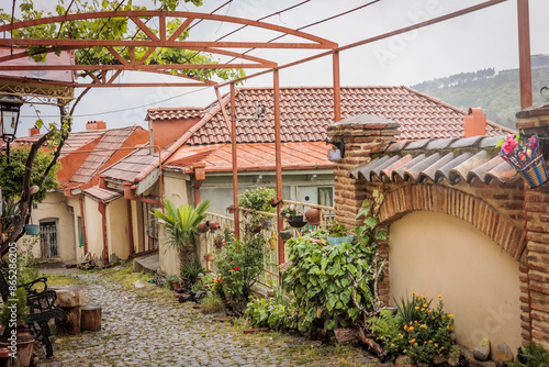 A small street in Sighnaghi with a stone pavement, surrounded by houses with red tiled roofs and greenery. The spring rain adds atmosphere and freshness to this cozy corner of the old Georgian town. photo