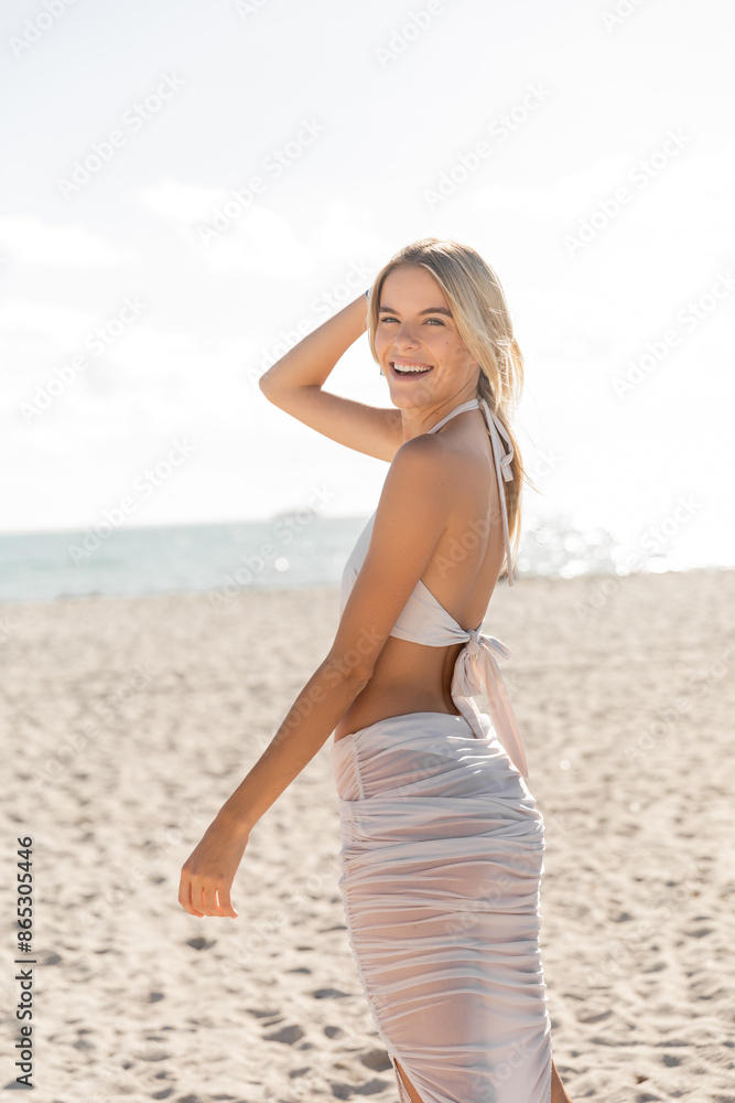A young, blonde woman stands gracefully on a sandy Miami beach, taking in the beauty of the horizon and the vast ocean. A young, blonde woman stands gracefully on a sandy Miami beach, taking in the beauty of the horizon and the vast ocean.