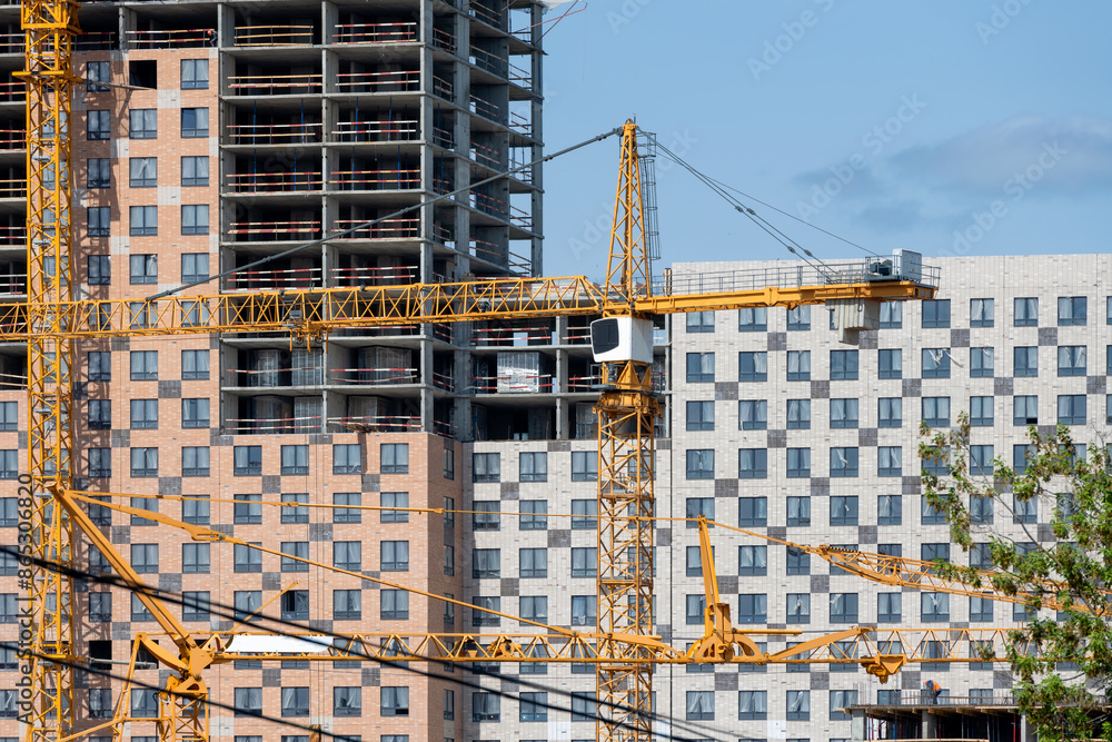 Tower cranes in close-up against the background of a multi-storey building under construction Tower cranes in close-up against the background of a multi-storey building under construction