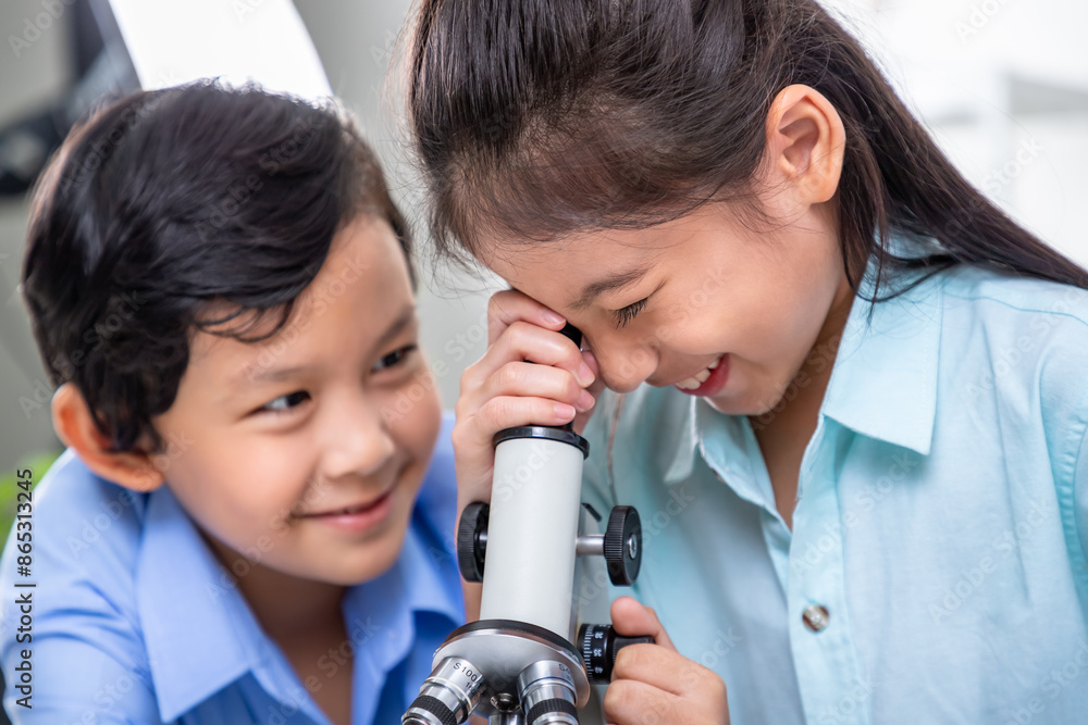 Asian young pupils smiling while examining specimen with microscope in science class Asian young pupils smiling while examining specimen with microscope in science class