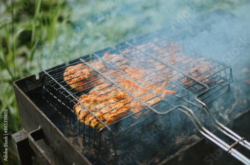 Wallpaper Mural A young man is cooking juicy meat with smoke on a grill in nature on a lake in summer Torontodigital.ca