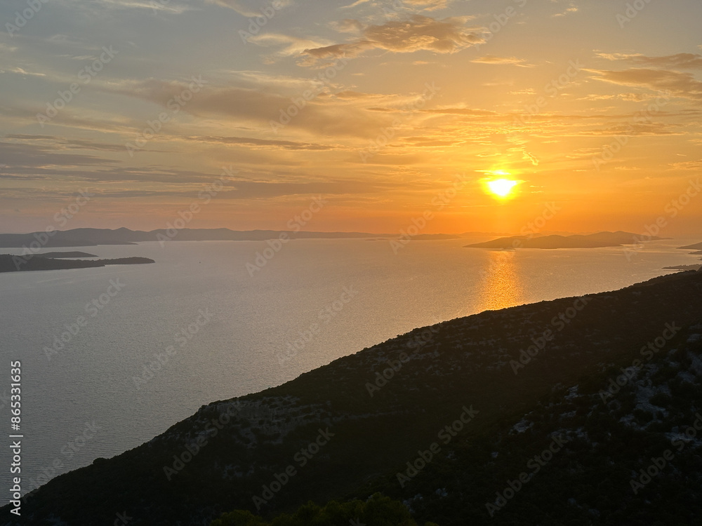 Fototapeta premium Reflection of the setting sun in sea water, view from the mountain. Sunset against the backdrop of the sea and mountains.
