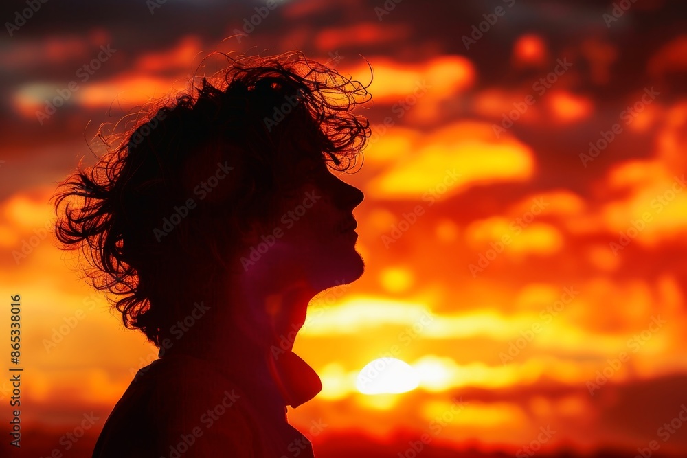 A person in profile standing against a vibrant sunset backdrop creating a golden silhouette. A person in profile standing against a vibrant sunset backdrop creating a golden silhouette.