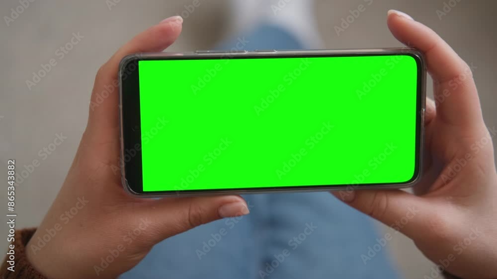 Young woman sitting at home holding smartphone green mock-up screen in hand. Female person use chroma key mobile phone. Horizontal mode. Touching, swipe display, tapping, surfing internet social media Young woman sitting at home holding smartphone green mock-up screen in hand. Female person use chroma key mobile phone. Horizontal mode. Touching, swipe display, tapping, surfing internet social media