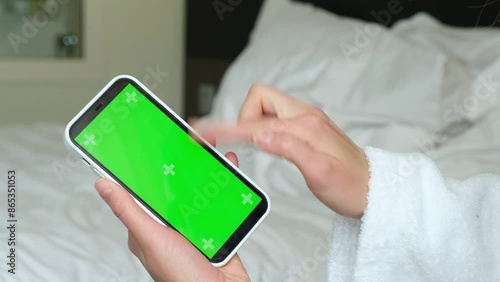 Phone screen. Bed background. Green screen. Shooting advertising. Close up of the chromakey phone screen. Close up of the hands. Scrolling ads. 4k video. High quality 4k footage photo