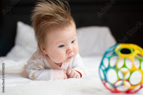 Little baby girl is playing with a toy during tummy time. 3 month old newborn baby development