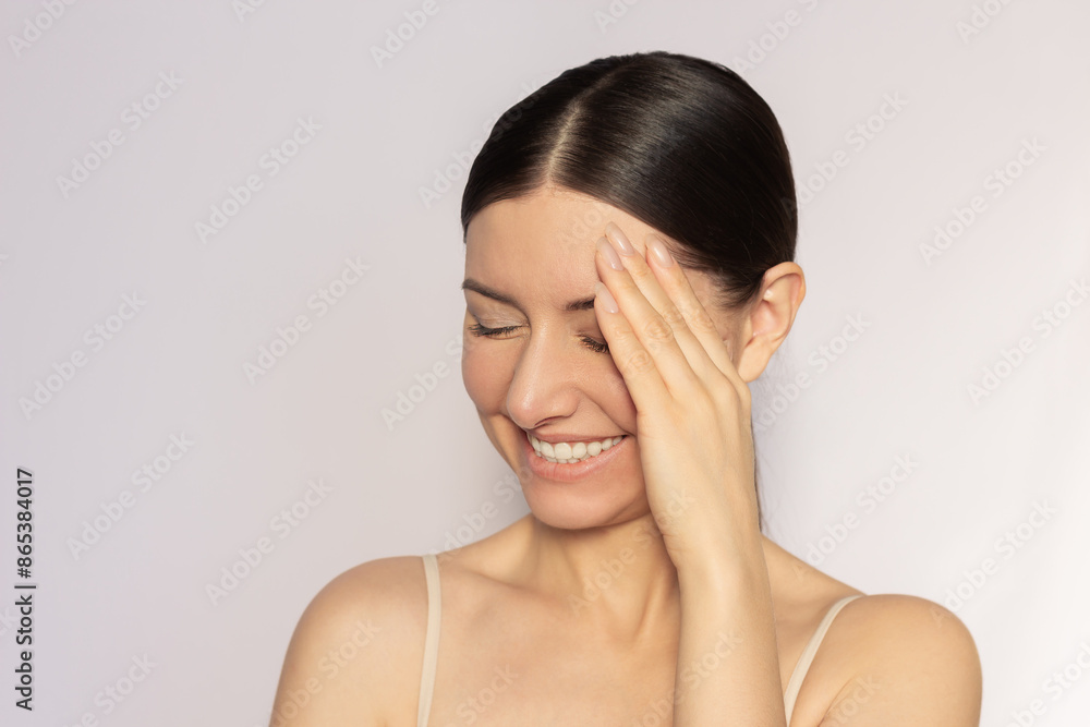 A young pretty Caucasian brunette woman smiles shyly and covers her face with her hand, closing her eyes. Expression of feelings and emotions. A young pretty Caucasian brunette woman smiles shyly and covers her face with her hand, closing her eyes. Expression of feelings and emotions.