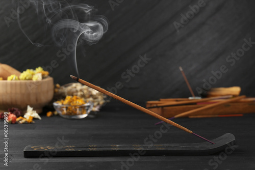 Aromatic incense stick smoldering in holder with om sign on black table