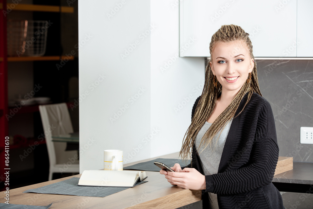 Young woman with dreadlocks is using smartphone in kitchen Young woman with dreadlocks is using smartphone in kitchen