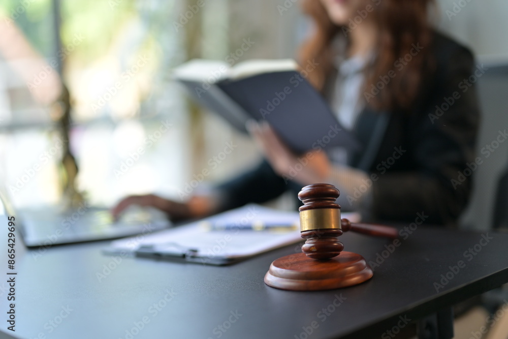 Lawyer working on a laptop while reading a law book, with a judge's gavel on the desk, exuding legal professionalism and dedication Lawyer working on a laptop while reading a law book, with a judge's gavel on the desk, exuding legal professionalism and dedication