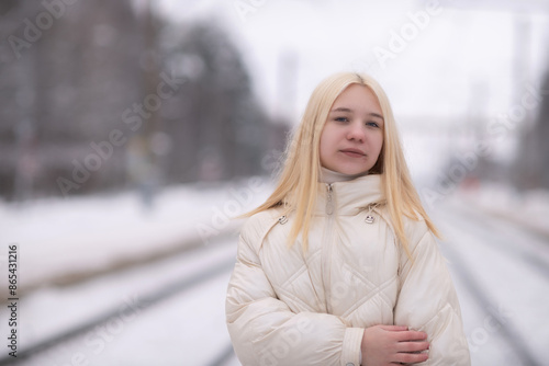 Portrait of a young beautiful blonde girl outdoors in winter in cloudy weather.