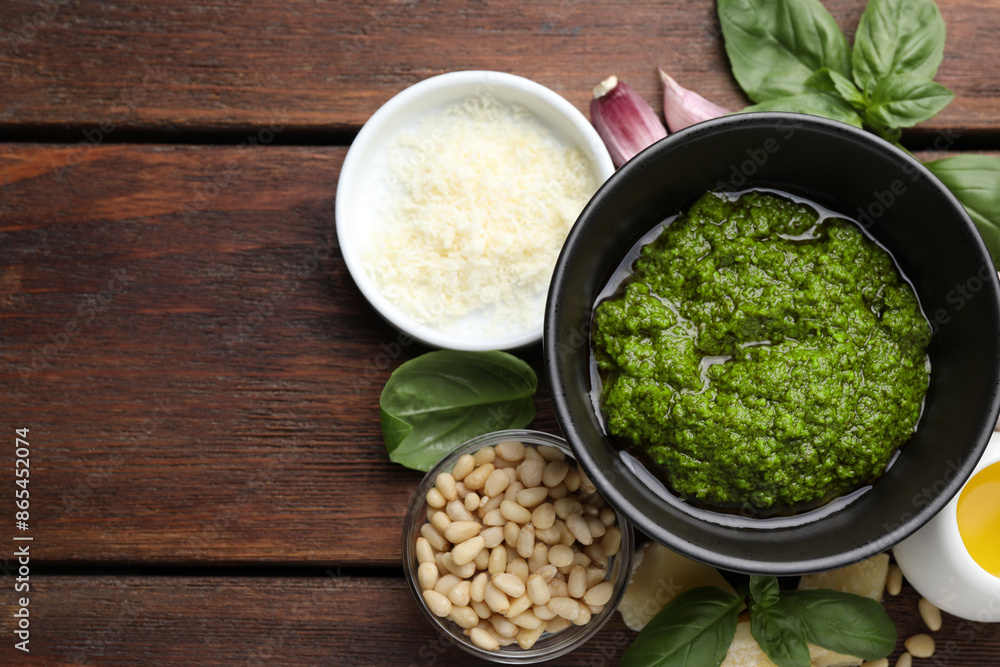 Tasty pesto sauce in bowl, basil, pine nuts, cheese, garlic on wooden table, top view. Space for text Tasty pesto sauce in bowl, basil, pine nuts, cheese, garlic on wooden table, top view. Space for text
