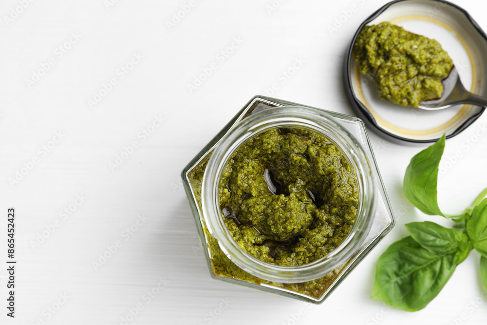 Tasty pesto sauce in jar, spoon and basil on white wooden table, top view. Space for text Tasty pesto sauce in jar, spoon and basil on white wooden table, top view. Space for text