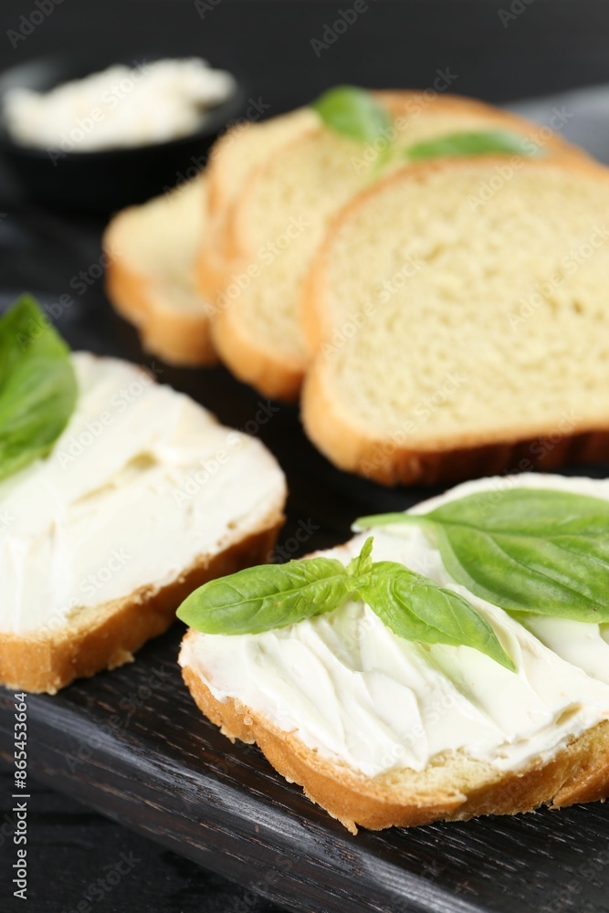 Pieces of bread with cream cheese and basil leaves on black table, closeup Pieces of bread with cream cheese and basil leaves on black table, closeup