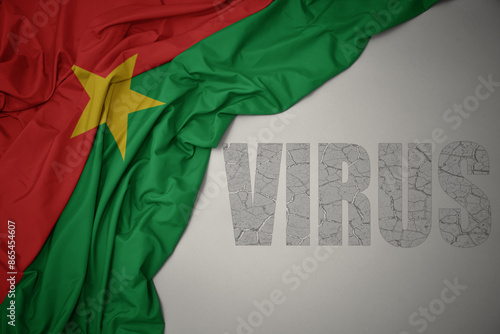 waving colorful national flag of burkina faso on a gray background with text virus .