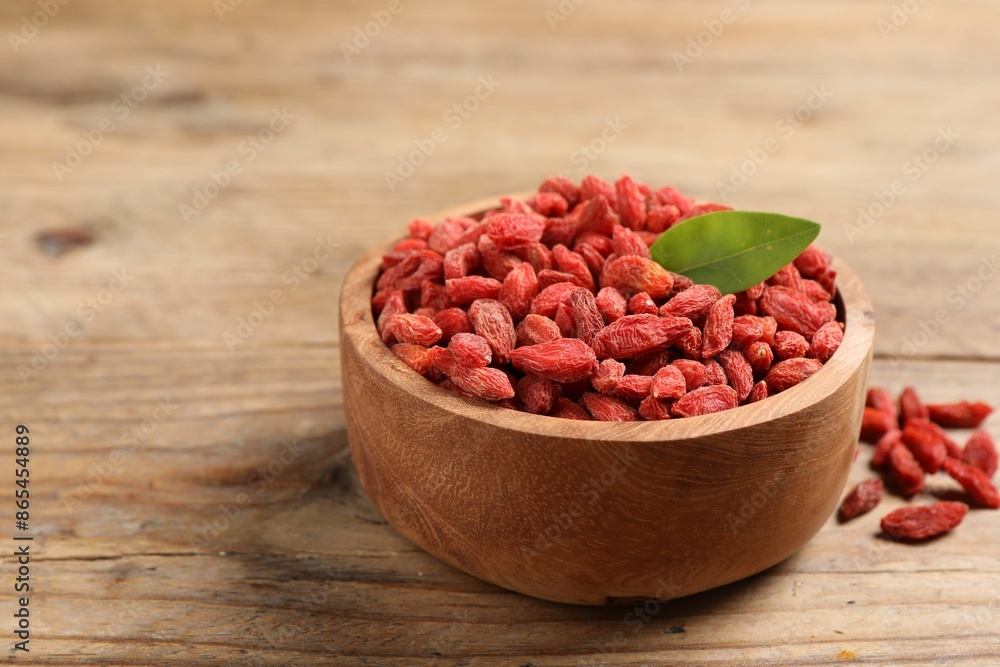 Dried goji berries and leaf in bowl on wooden table, closeup. Space for text Dried goji berries and leaf in bowl on wooden table, closeup. Space for text