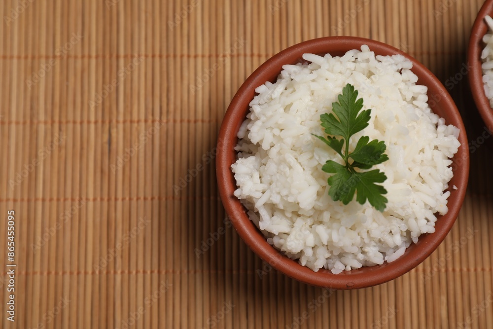 Bowls of delicious boiled rice with parsley on bamboo mat, top view. Space for text Bowls of delicious boiled rice with parsley on bamboo mat, top view. Space for text