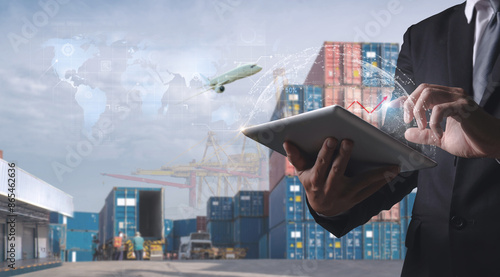 Businessman using tablet for digital logistics management with cargo containers, airplane, and global map overlay.
