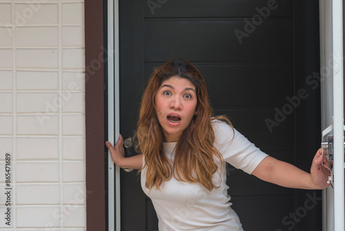 An angry Asian woman in her 30s is standing at her door, demanding someone to leave her apartment or property. Example of restraining order. Pov of estranged ex-husband. photo