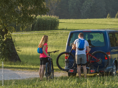 Couple on a nature recreational adventure, taking down electric mountain bikes from the bike rack on a van photo