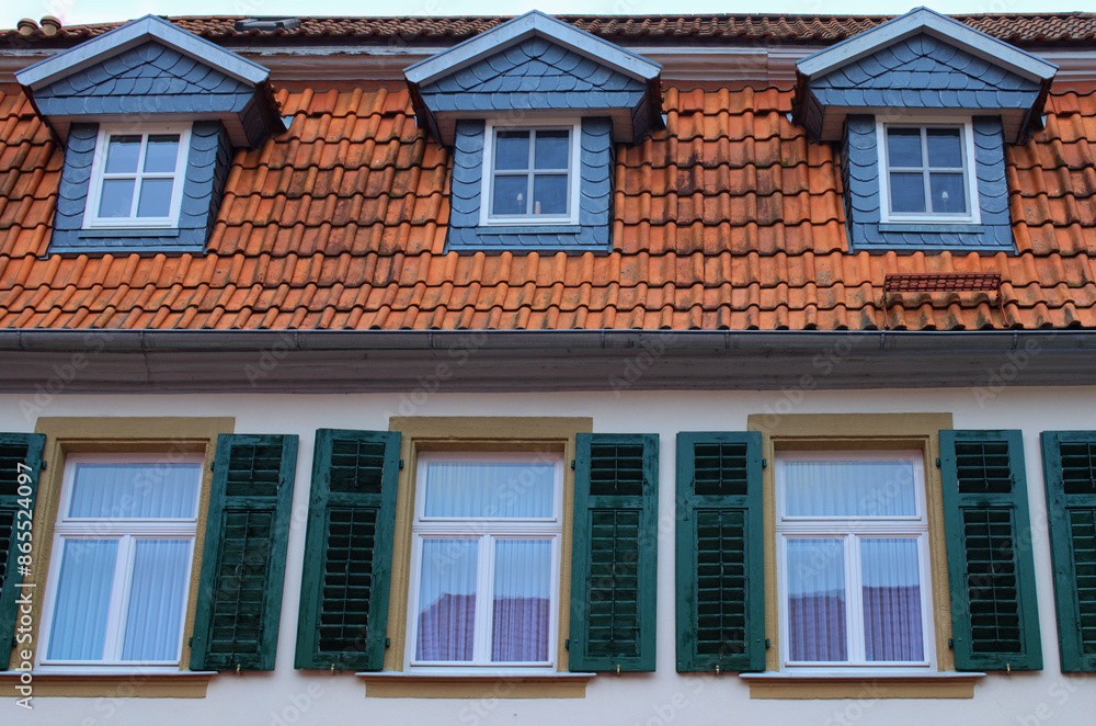 Fototapeta premium Close-up house. Three windows with green wooden shutters and the smaller windows in the red tile roof. Typical architecture in Bavaria, region Upper Franconia, Germany. Travel and tourism concept