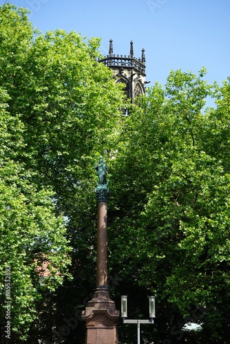 Die Mariensäule auf dem Marienplatz vor üppigem Grün und dem Kirchturm der katholischen Pfarrkirche St. Ludgeri im Sommer bei blauem Himmel und Sonnenschein in Münster in Westfalen im Münsterland photo