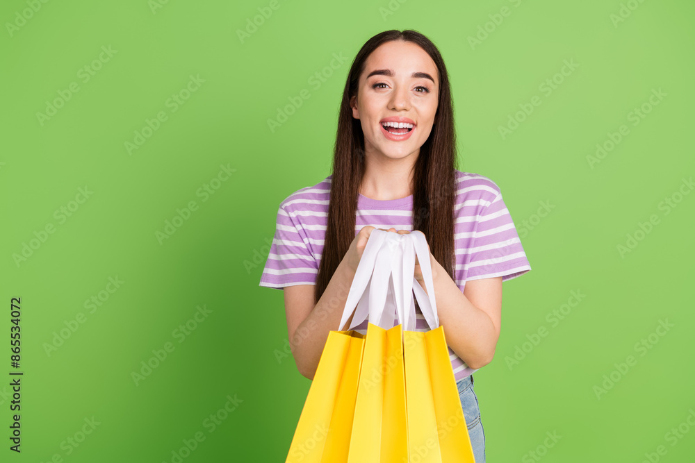 Photo portrait of pretty young girl hold shopping bags wear trendy striped violet outfit isolated on green color background Photo portrait of pretty young girl hold shopping bags wear trendy striped violet outfit isolated on green color background