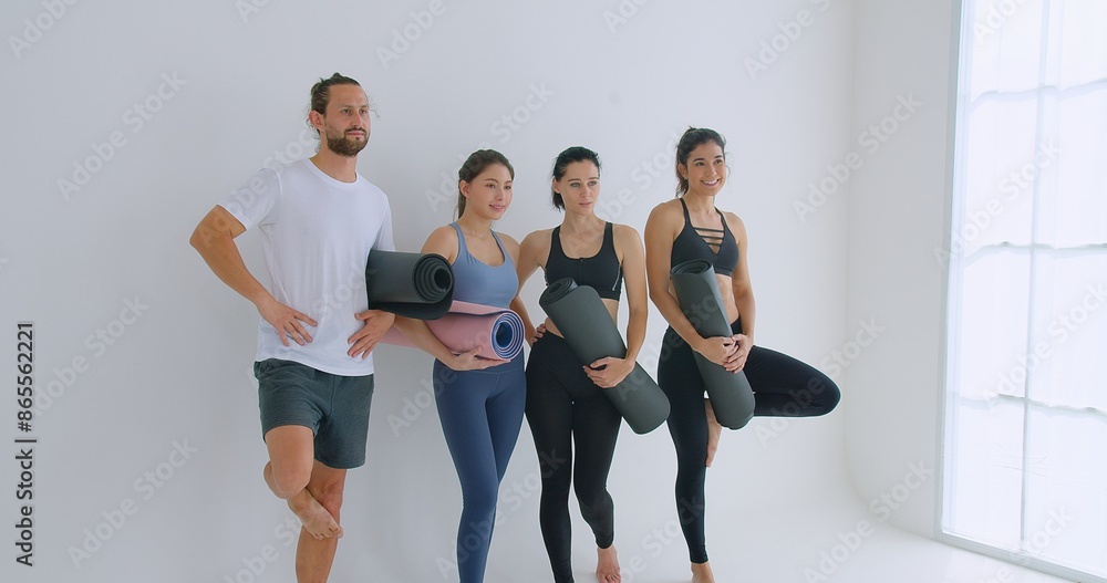 Obraz premium Group of Young Adults Posing with Yoga Mats in Minimalist Studio, Ready for a Yoga Session, Dressed in Athletic Wear, Smiling and Relaxed, Emphasizing Health, Fitness, and Well-being