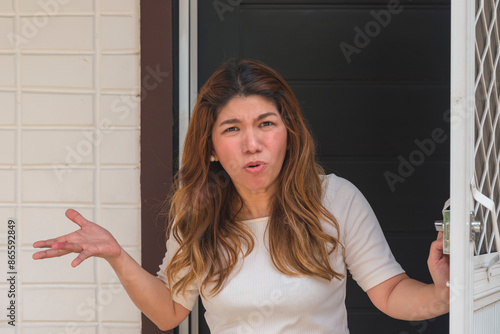 An Asian woman in her 30s protesting, complaining while standing at her door, reacting to increased rent and bills.