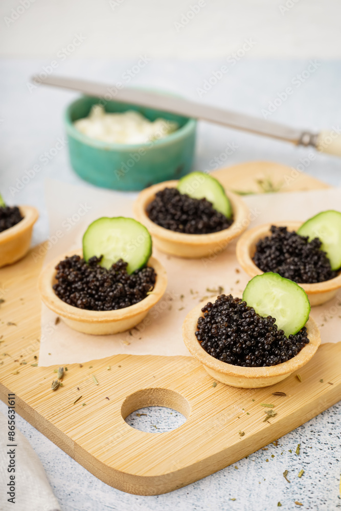 Wooden board of tasty tartlets with black caviar on grey background Wooden board of tasty tartlets with black caviar on grey background