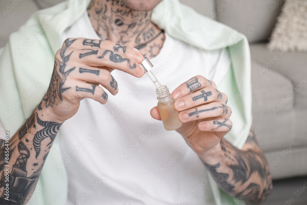Young tattooed man with bottle of CBD oil at home, closeup Young tattooed man with bottle of CBD oil at home, closeup