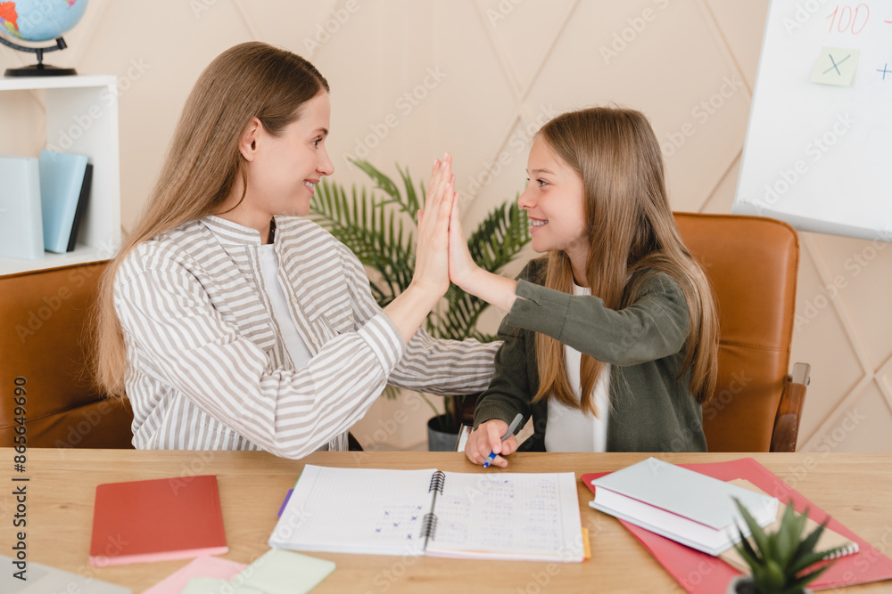 Successful young tutor teacher mother babysitter nanny helping her daughter student schoolgirl with homework, test, exam, new topic giving high five at home school. Successful young tutor teacher mother babysitter nanny helping her daughter student schoolgirl with homework, test, exam, new topic giving high five at home school.