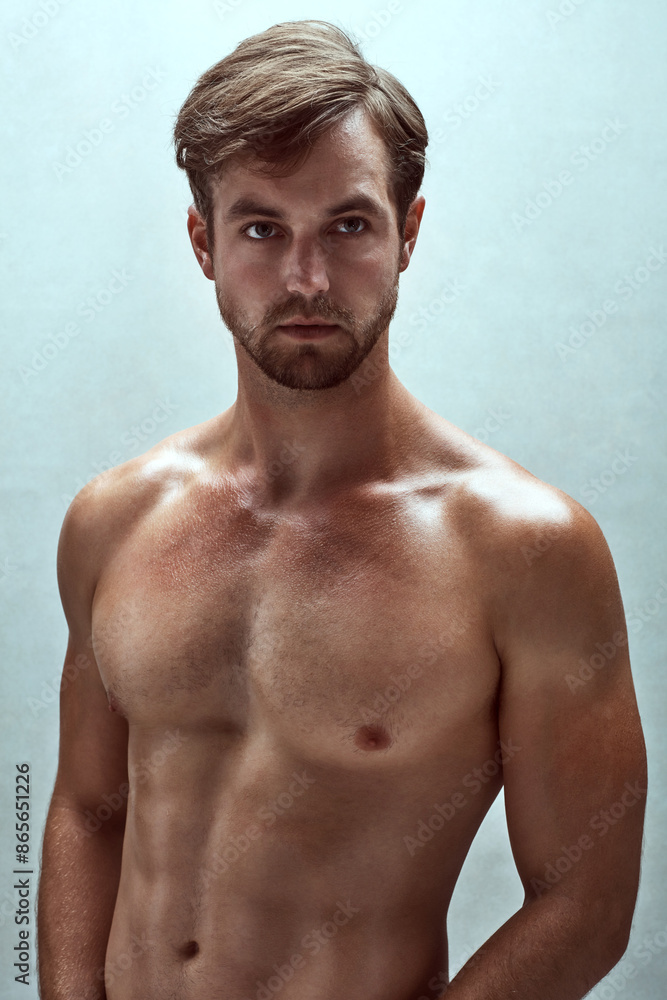 Fototapeta premium Man, stomach and shirtless exercise in studio, strong abs and muscle on blue background. Male person, confident and athlete for power training or healthy body, bodybuilder and topless for wellness