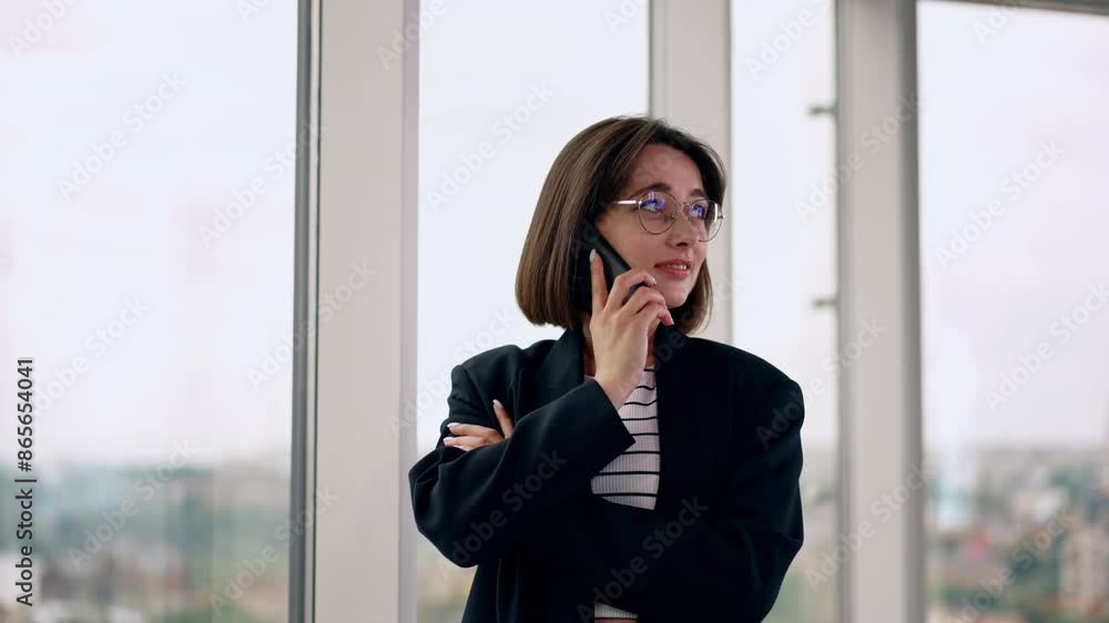 Caucasian brunette having phone conversation indoors. Portrait of a positive lady in glasses speaking on the smartphone near the window. Caucasian brunette having phone conversation indoors. Portrait of a positive lady in glasses speaking on the smartphone near the window.