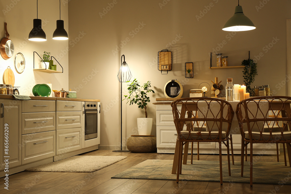 Interior of modern kitchen with glowing lamps, white counters, chairs and dining table at evening Interior of modern kitchen with glowing lamps, white counters, chairs and dining table at evening